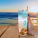 Woman holding seashell tumbler outdoors at table with beach view

